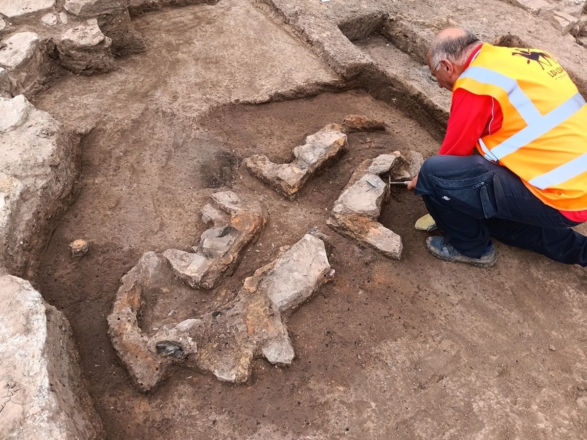 Ein Archäologie kniet vor den steinernen Strukturen einer Glockengussanlage