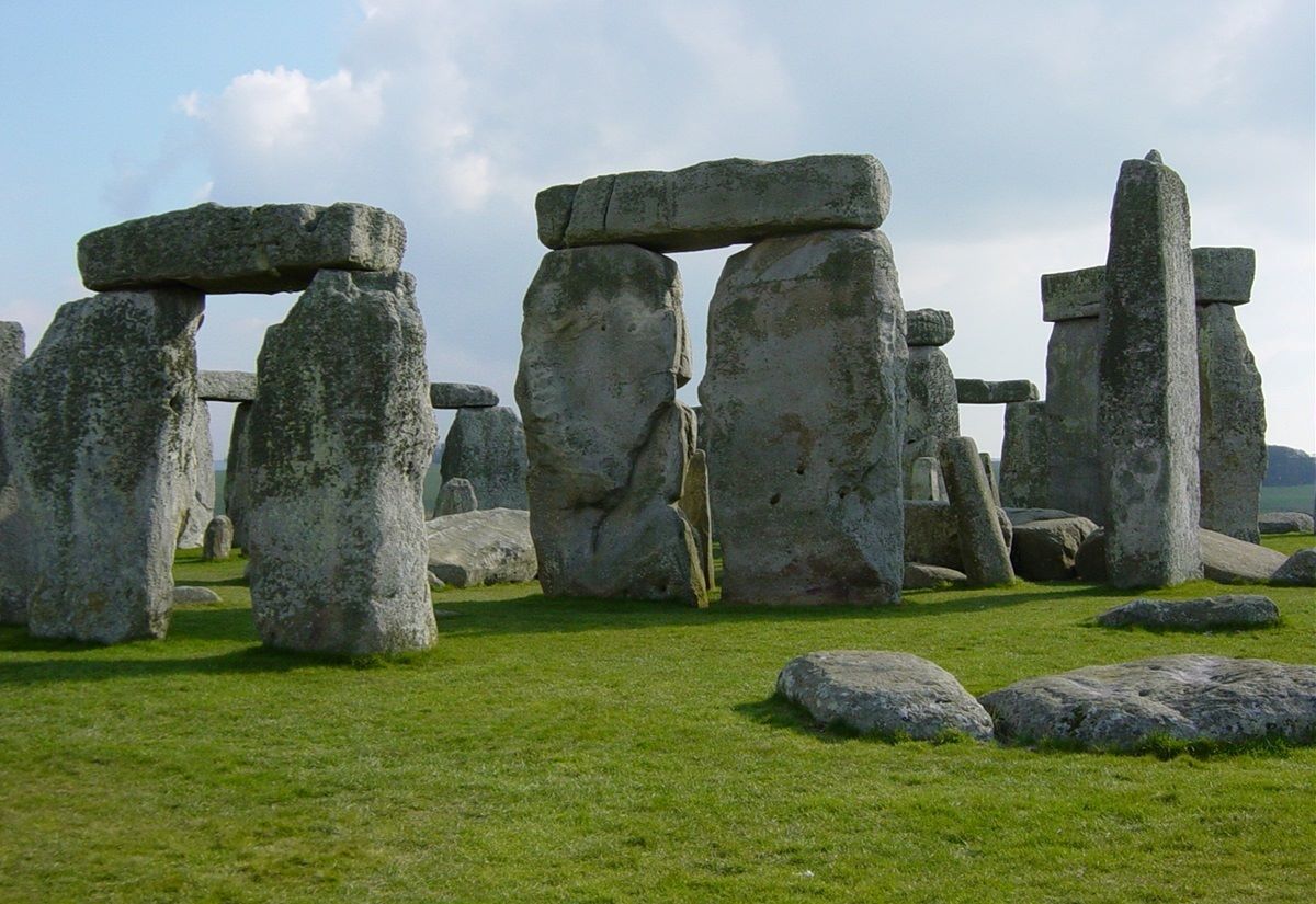 Steinmonument Stonehenge mit aufrecht stehenden und horizontal liegenden großen Steinen auf grünem Gras unter bewölktem Himmel