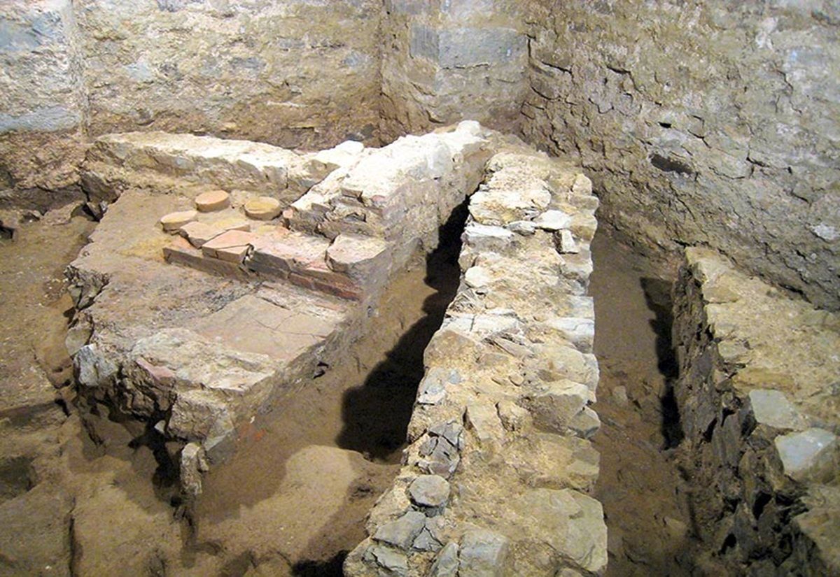 Archäologische Ausgrabungsstätte mit freigelegten Steinmauern und Bodenplatten in einem Raum