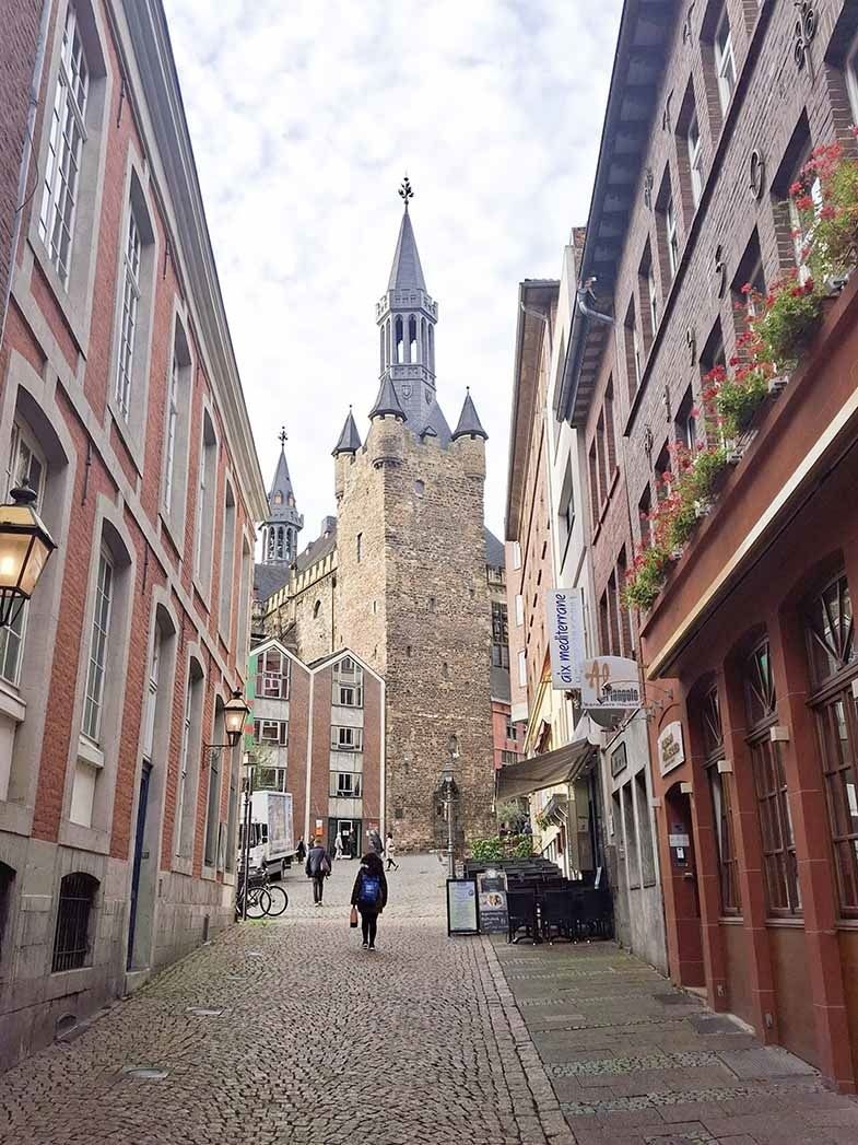 Blick auf den mittelalterlichen Turm in Aachen, gepflasterte Straße mit Fußgängern und historischen Gebäuden links und rechts