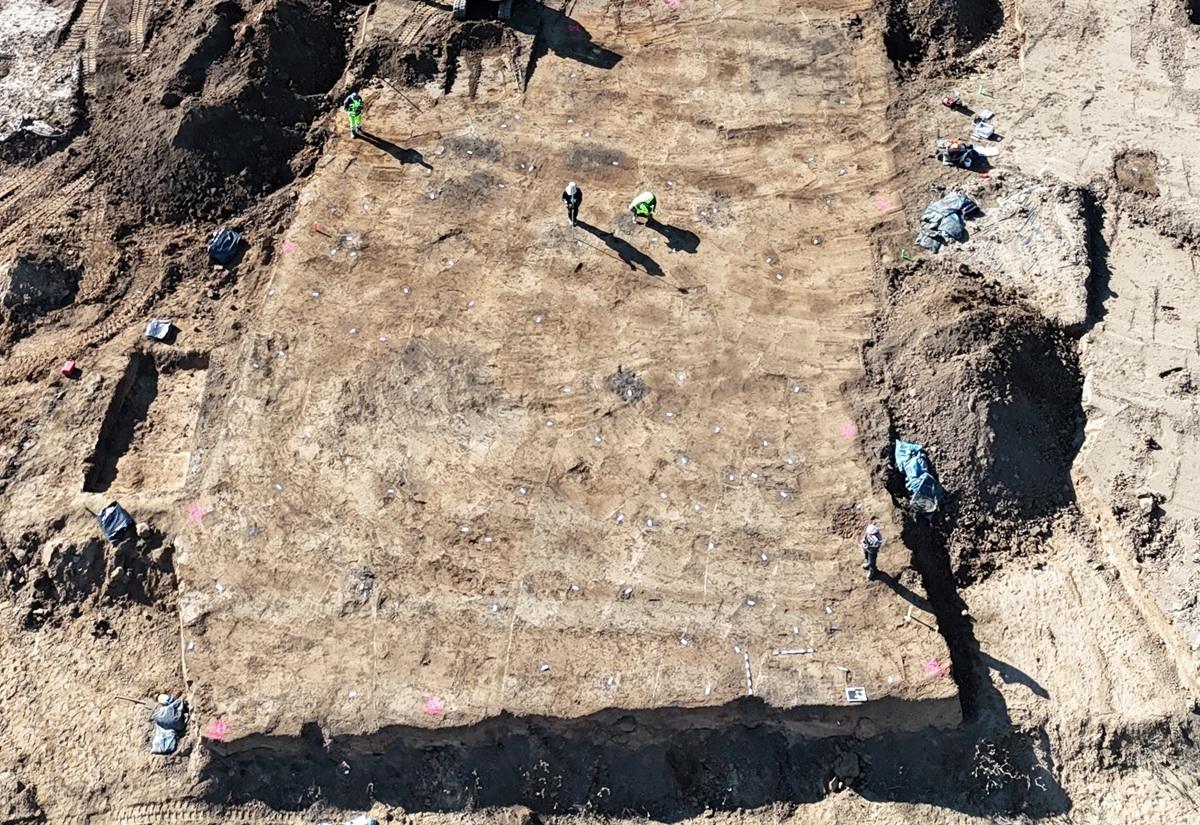 Luftaufnahme einer archäologischen Ausgrabungsstätte mit mehreren Personen auf einem rechteckigen Erdareal