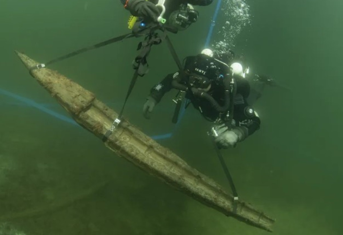 Zwei Taucher heben eine lange, hölzerne Geschützplattform aus dem Wrack der Gribshunden unter Wasser mit Hebegurten
