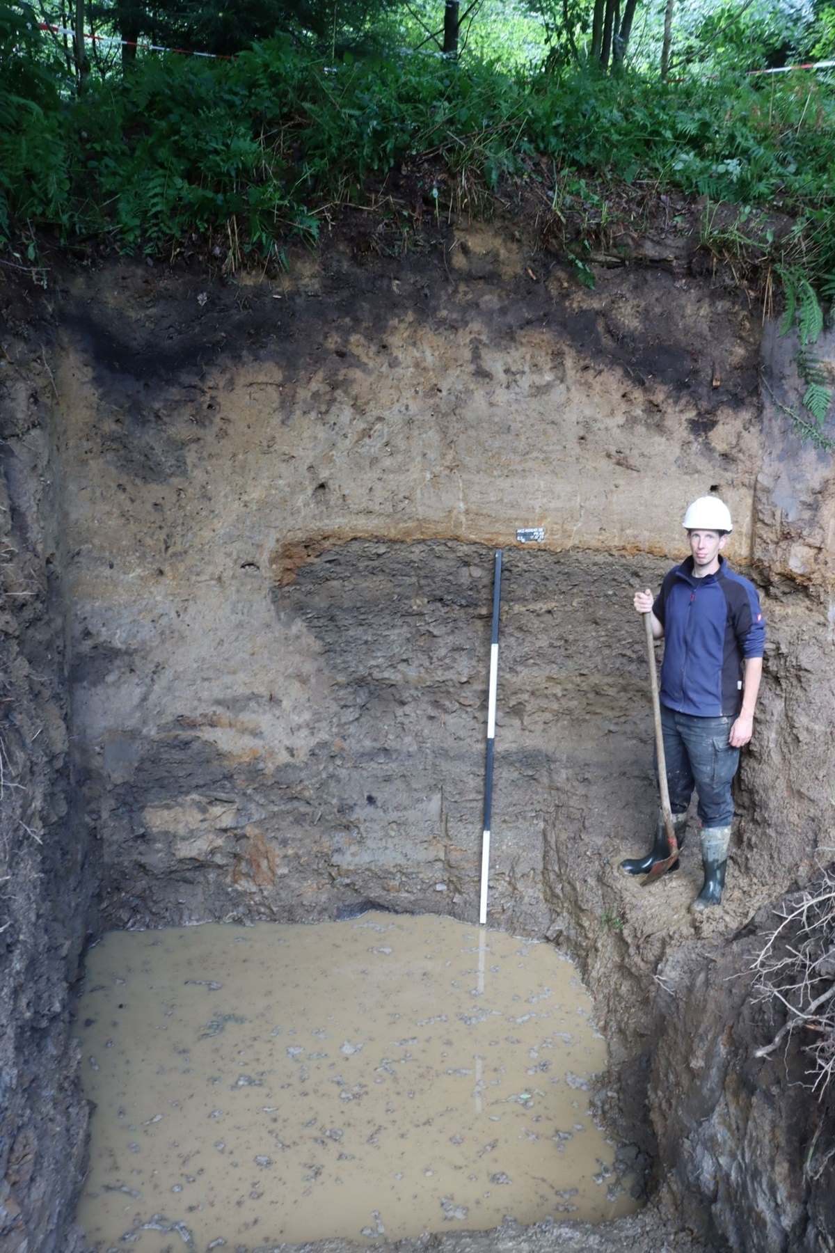 Ein Archäologe steht neben dem im Profil sichtbaren Stollenmundloch