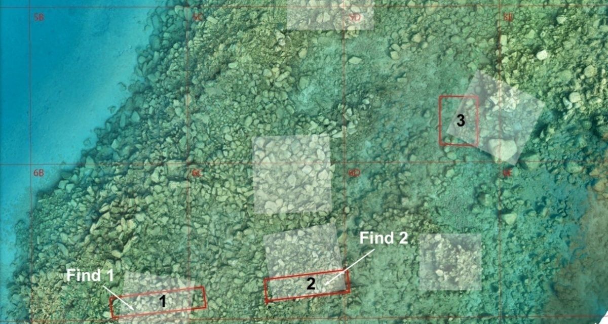Luftaufnahme eines küstennahen, flachen Meeresbereichs mit grünlich-türkisem Wasser. Der Meeresboden ist von zahlreichen Steinen und Felsen bedeckt. Mehrere rechteckige Bereiche sind mit roten Linien markiert und nummeriert. In zwei Feldern steht jeweils der Text 'Find 1' und 'Find 2', daneben die Zahlen '1', '2' und '3'. Die Markierungen heben bestimmte Fundstellen hervor.