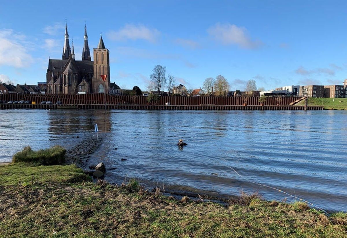 Fluss mit einem Taucher im Wasser, im Hintergrund ein moderner Kai und eine Kirche mit zwei hohen Türmen unter blauem Himmel.
