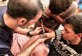 Tätowierer sticht einem Jungen ein Tattoo der Jungfrau Maria.